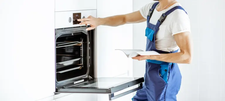 Handsome workman in overalls setting up electric oven on the kitchen at home