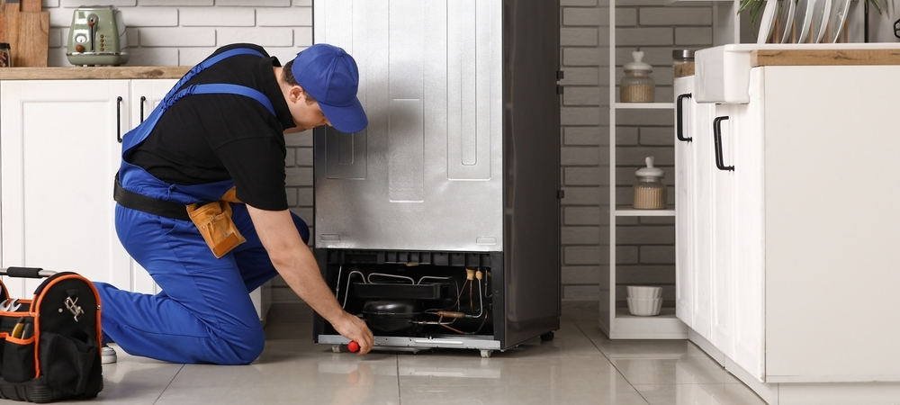 Repairing refrigerator in the kitchen Male appliance repair technician with tools repairing refrigerator in the kitchen