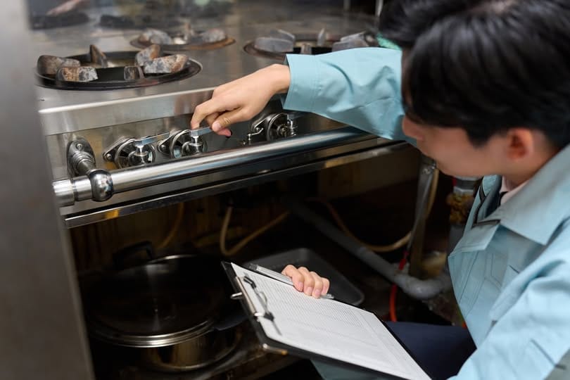 A man checking a gas stove at a restaurant