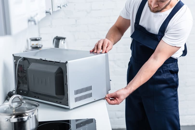 partial view of adult handyman repairing microwave oven in kitchen