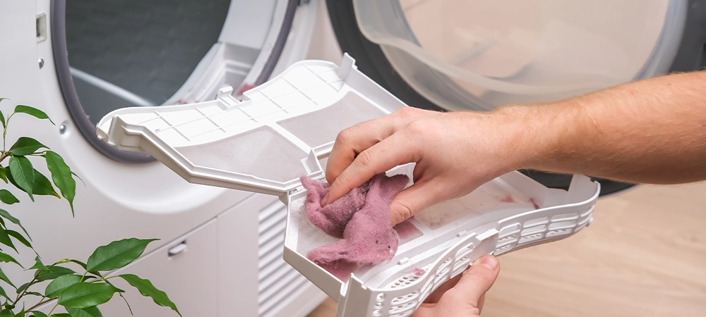 A man holds a dirty dryer filter. A man collects lint, hair, wool from the filter of a drying machine. Red lint on the dryer filter. Dirty filter dryer.