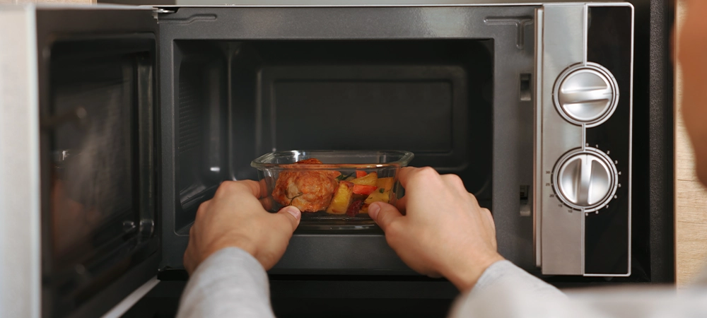 microwave cooking times Man putting container with lunch into microwave in kitchen, closeup