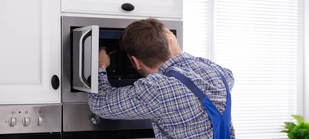 Side View Of Young Man Repairing Microwave Oven In Kitchen