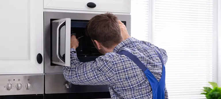 Side View Of Young Man Repairing Microwave Oven In Kitchen