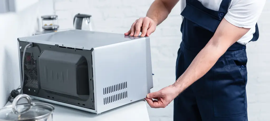 partial view of adult handyman repairing microwave oven in kitchen