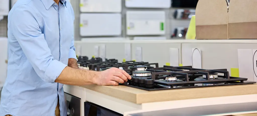 A man is carefully inspecting a sleek gas stove in a contemporary appliance showroom, which is showcasing a variety of modern kitchen features and advanced technology designed for cooking