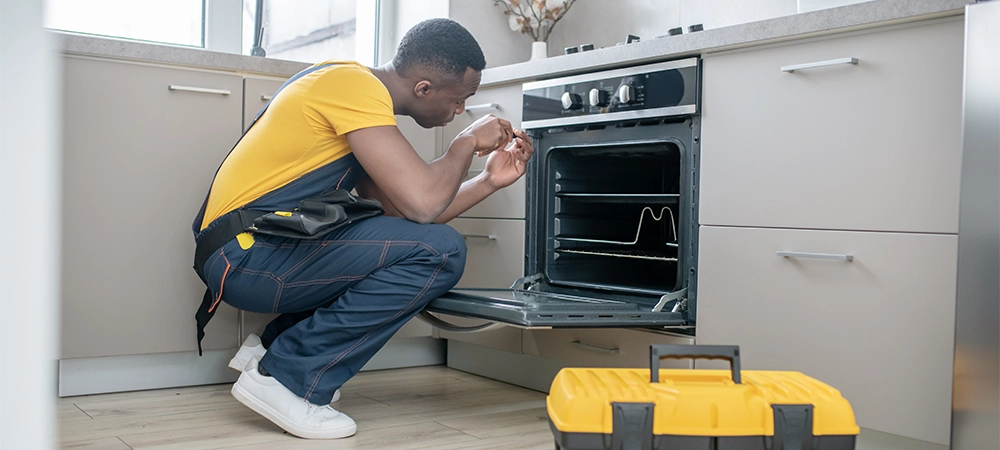 Gas stove repair. Dark-skinned service man in yellow tshirt repairing the gas stove