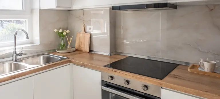 A kitchen interior with wooden countertop and cooking stove. Counter top in modern white kitchen. Style kitchen vanity sink with wood cabinets and black electric stove top