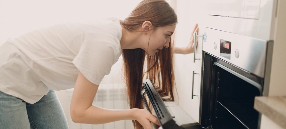 oven gas smell or electrical burning odor A housewife woman cooks food and looks into the oven in the kitchen