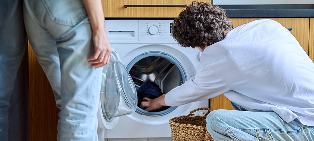 Young guy at home using washing machine with basket of dirty things