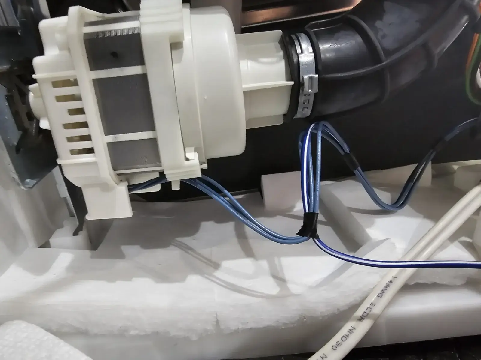 appliance repair close up white plastic pump blue wires black hose inside machin