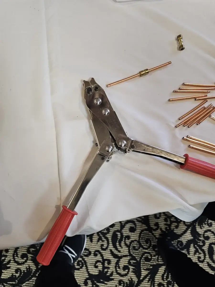 appliance repair metal crimping tool red handles rests near copper pipes fitting