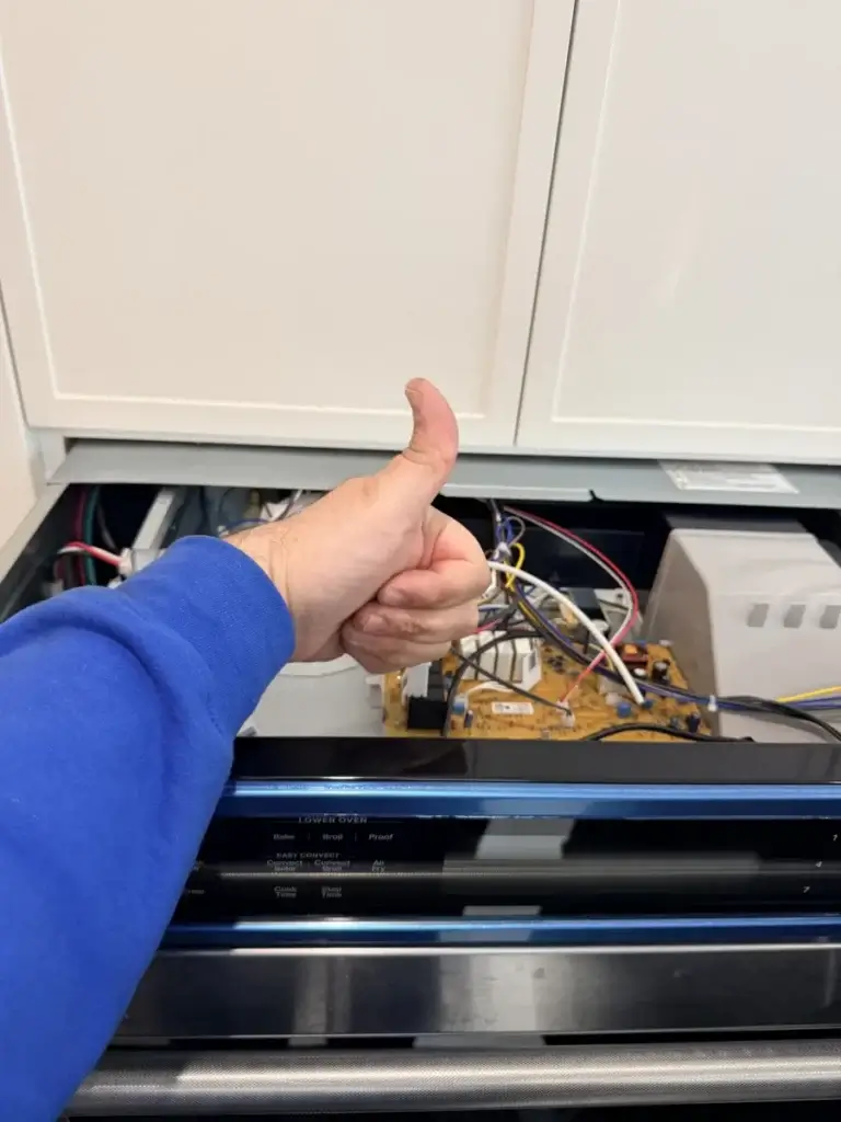 appliance repair person blue sleeve gives thumbs up while doing appliance repair