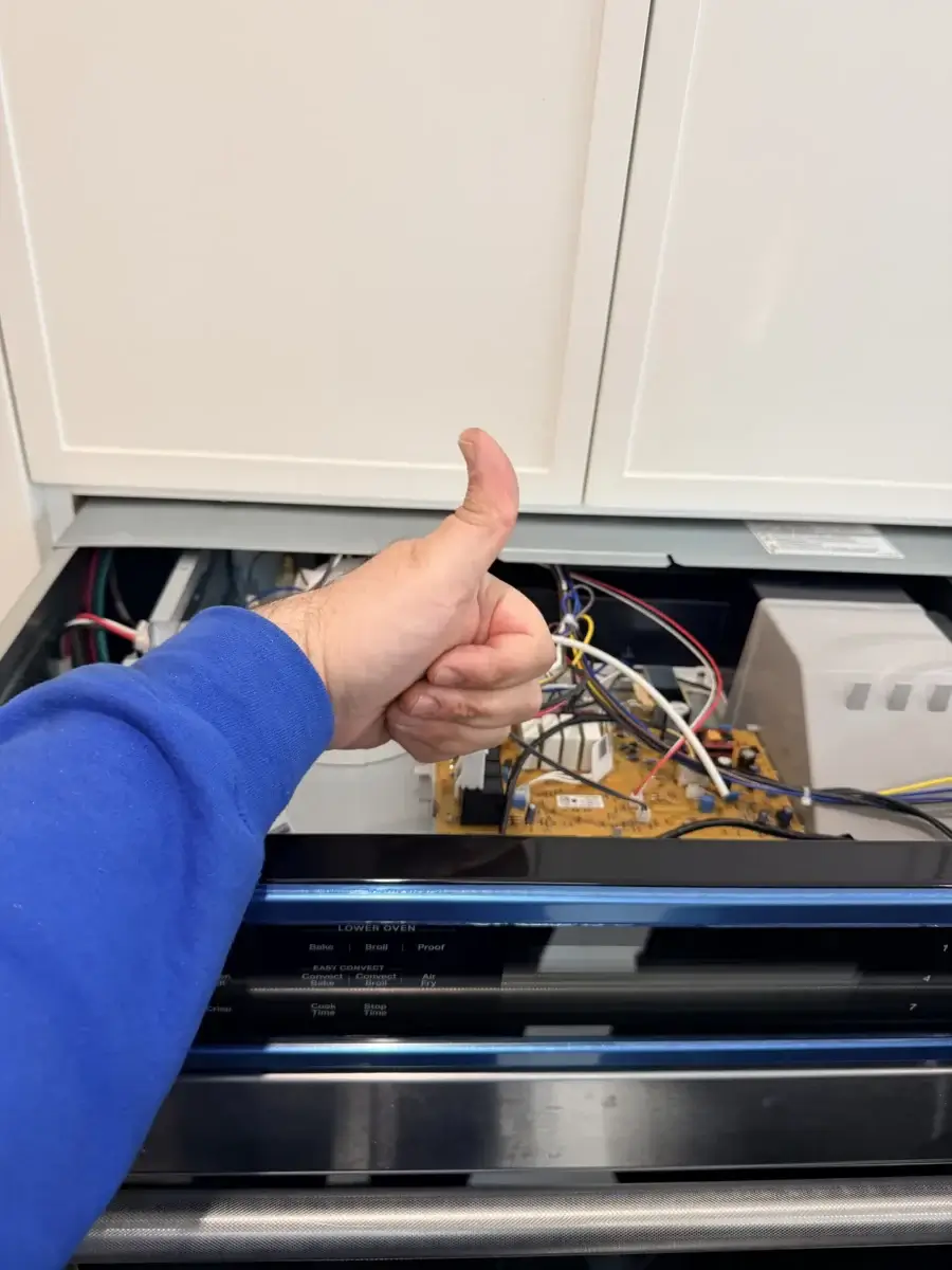 appliance repair person blue sleeve gives thumbs up while doing appliance repair