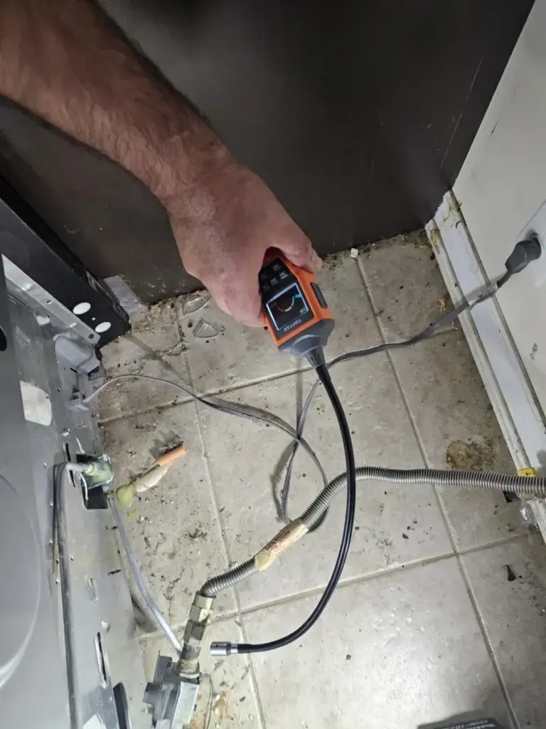Technician using a handheld tester behind an appliance during a diagnostic visit