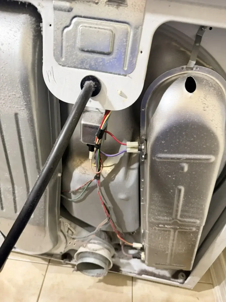 Back view of an open clothes dryer cabinet showing the heating element housing, vent outlet, electrical wiring, and access points for thermal fuse and high-limit thermostat replacement