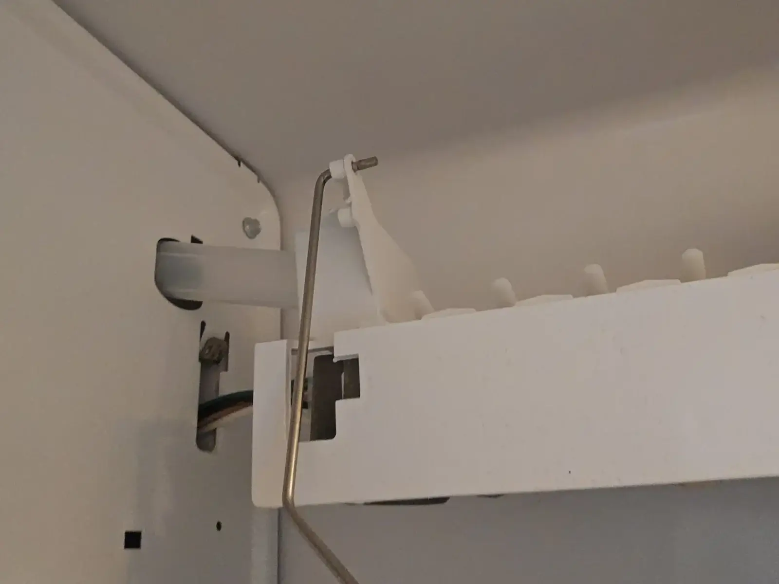 Close-up of an ice maker inside a freezer showing the metal shut-off arm and the ice tray