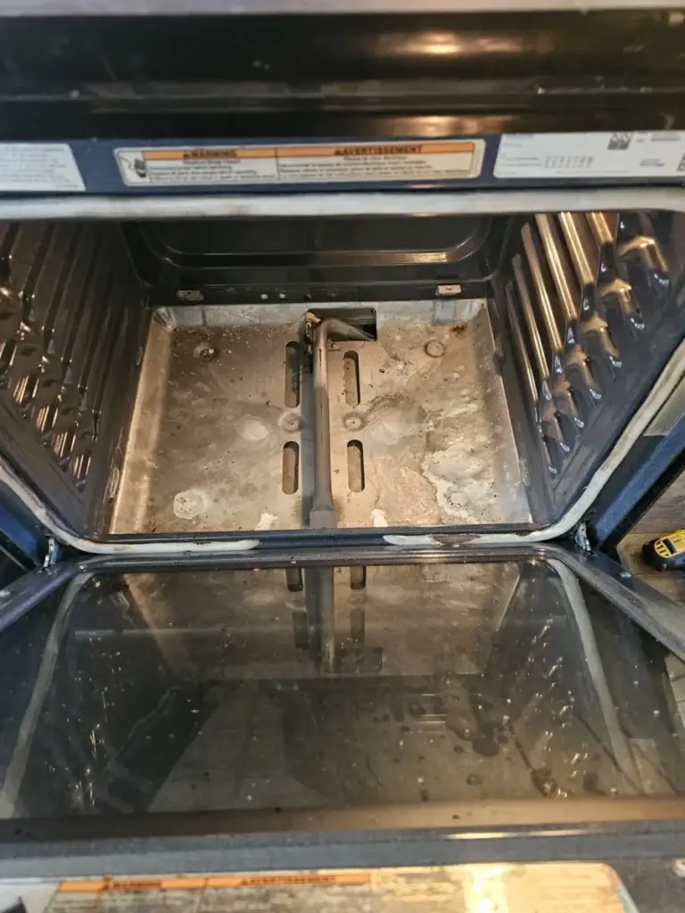 Inside a gas oven with the bottom panel removed, showing the bake burner area due for service