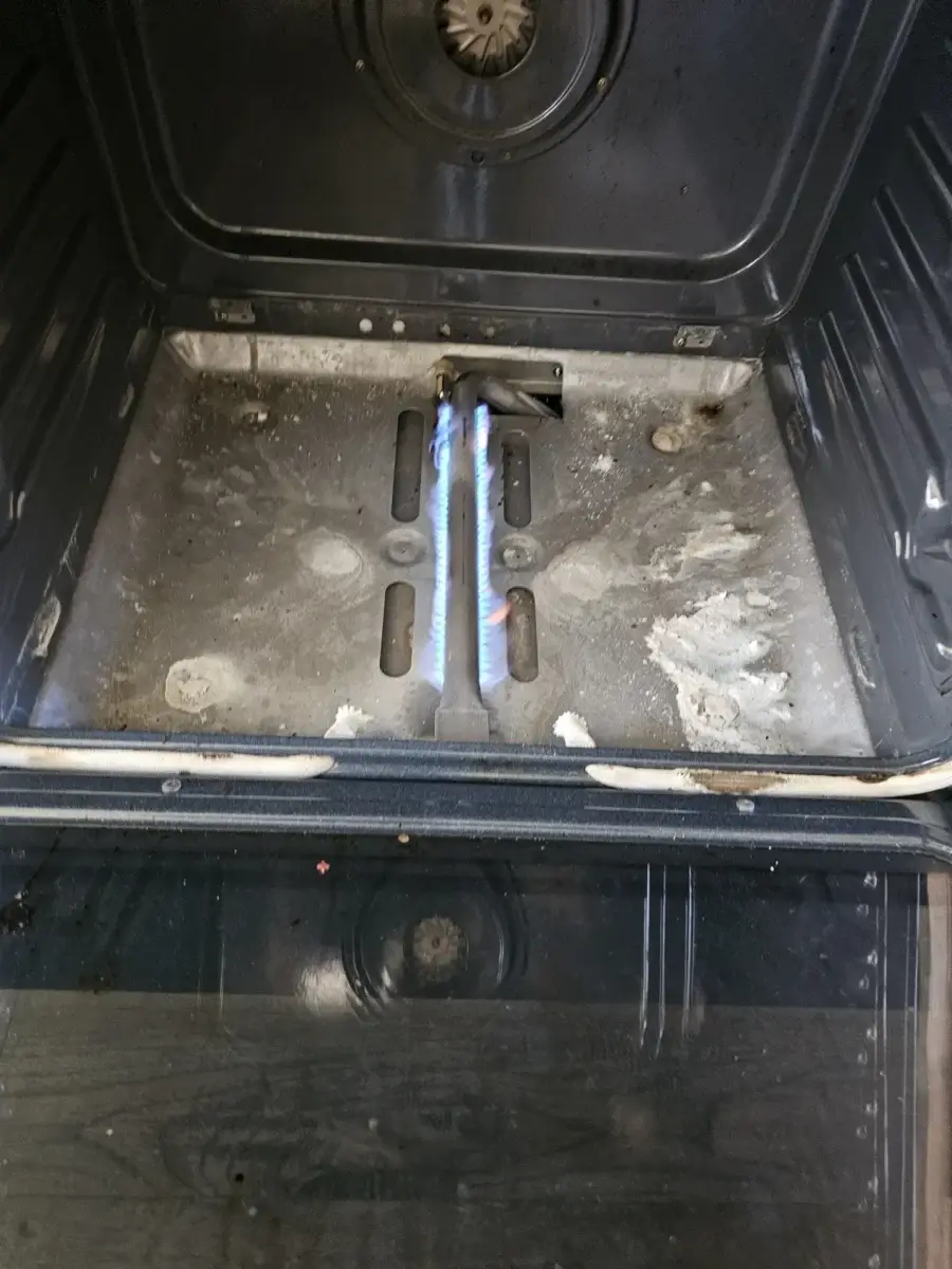 oven repair open oven door revealing lit blue gas burner grime around call appli