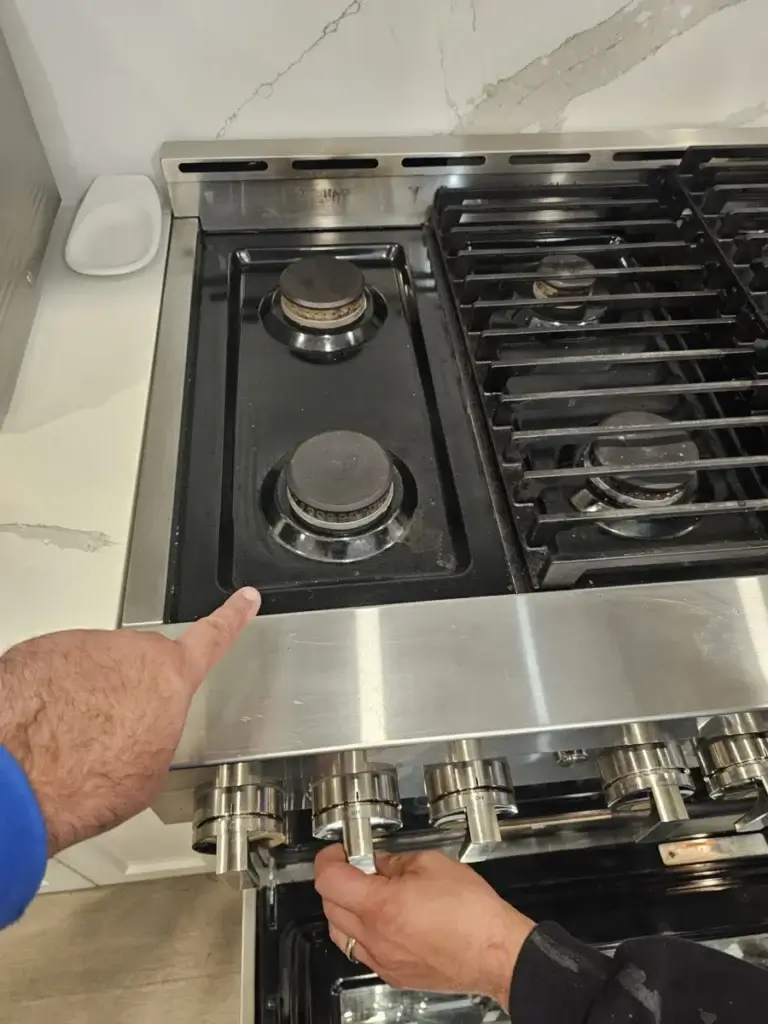Technician removing the stainless cover of a gas range to access the burners during installation