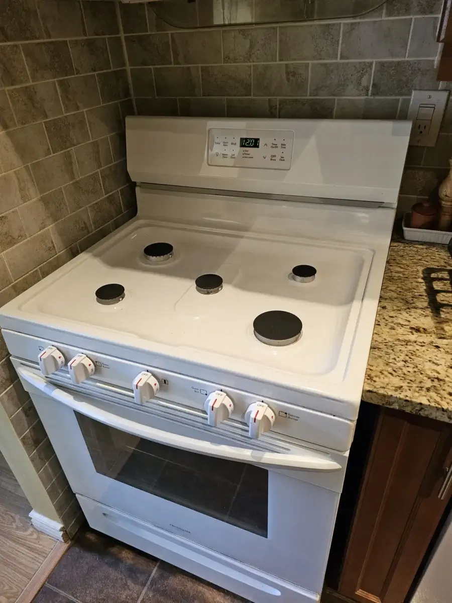 White electric stove with four burners, control knobs, and a digital clock — the typical unit behind an oven repair cost question in the GTA