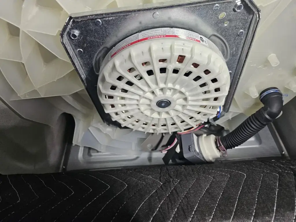 Underside of a washing machine tub showing the drive motor and drain hose, where balance problems are diagnosed