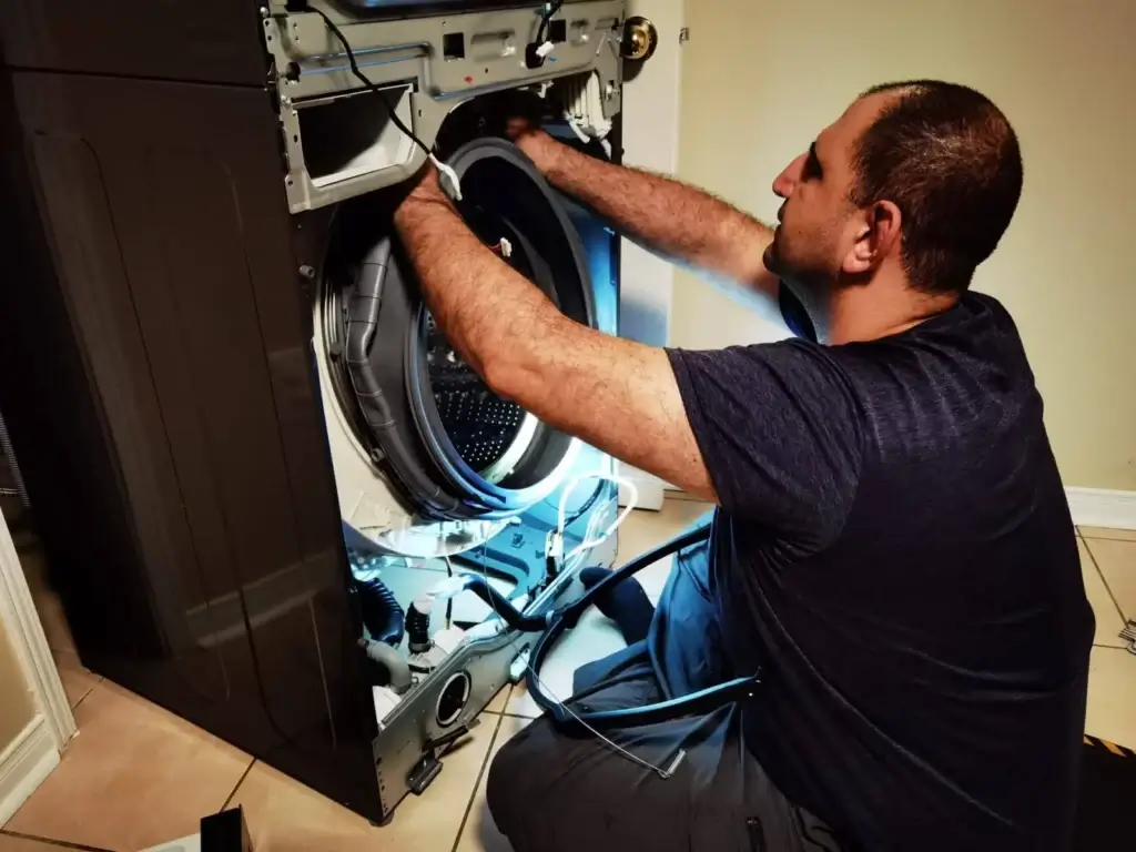 Appliance Forever technician repairing a front-load washer with the front panel removed to reach the drain pump