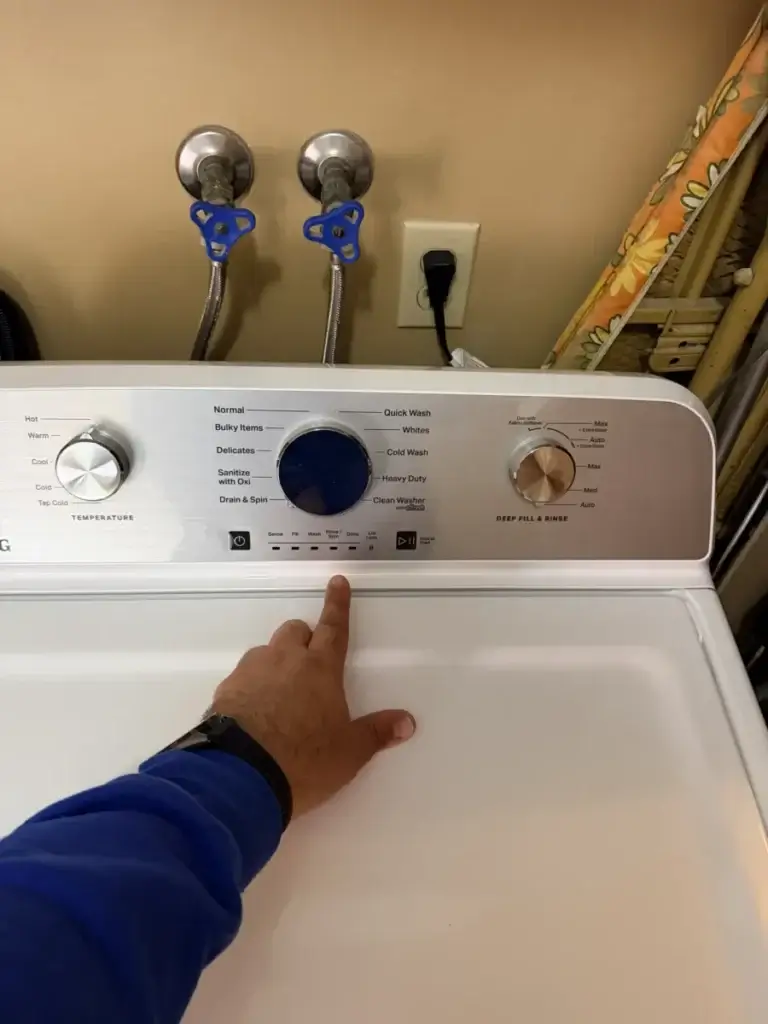 Technician pointing at the control panel of a top-load washer where the error code appears