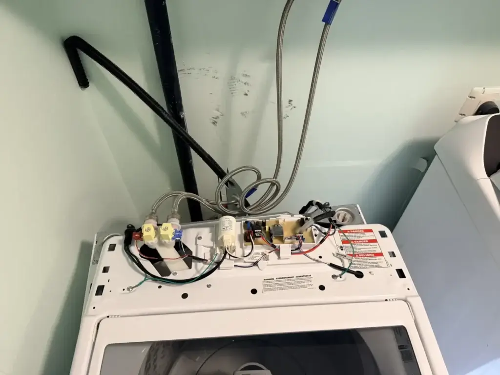 Top of a washing machine opened to show the water-inlet valves and fill hoses