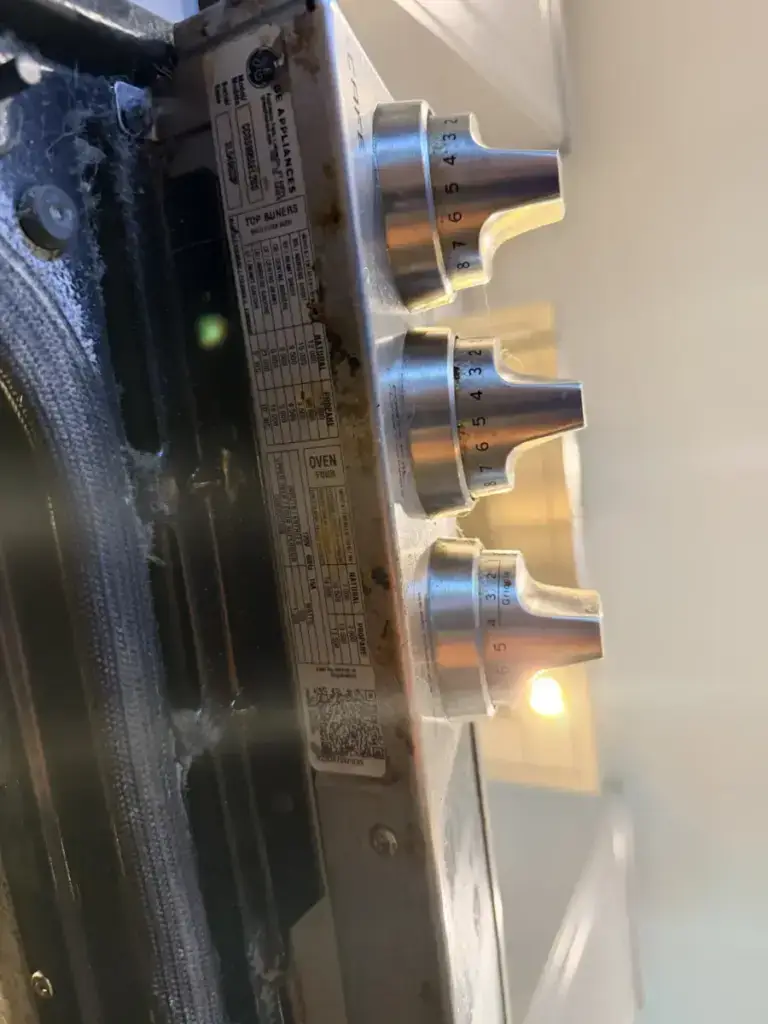 Close-up of GE gas range burner knobs and the appliance model rating label