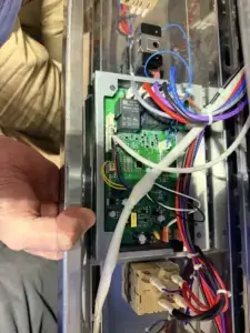 Technician holding an appliance control board with its wiring harness exposed during a repair