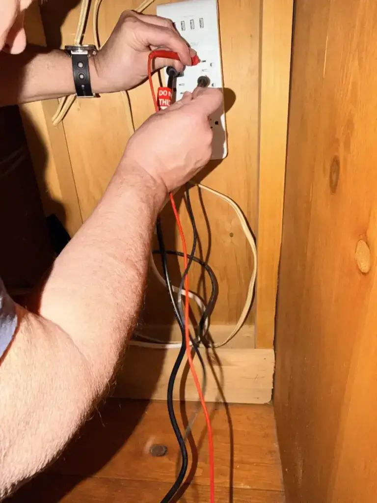 Appliance technician using a multimeter to test wiring at a wall outlet during an appliance repair diagnostic