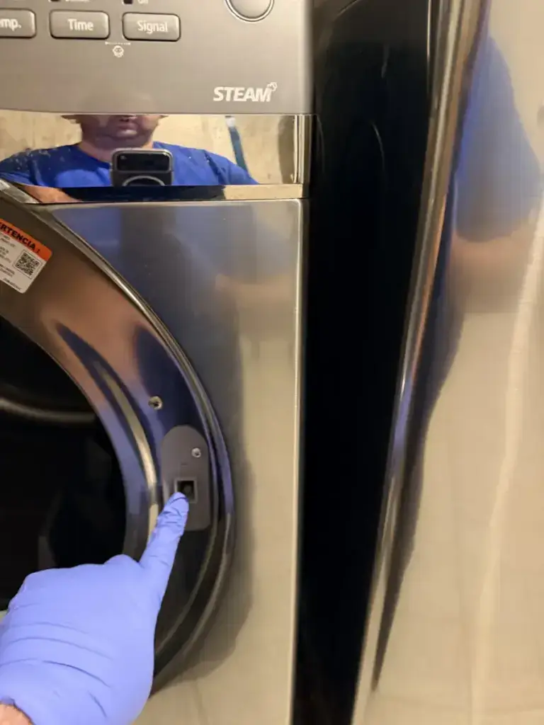 A gloved technician pointing at the lint filter housing of a stainless Samsung dryer