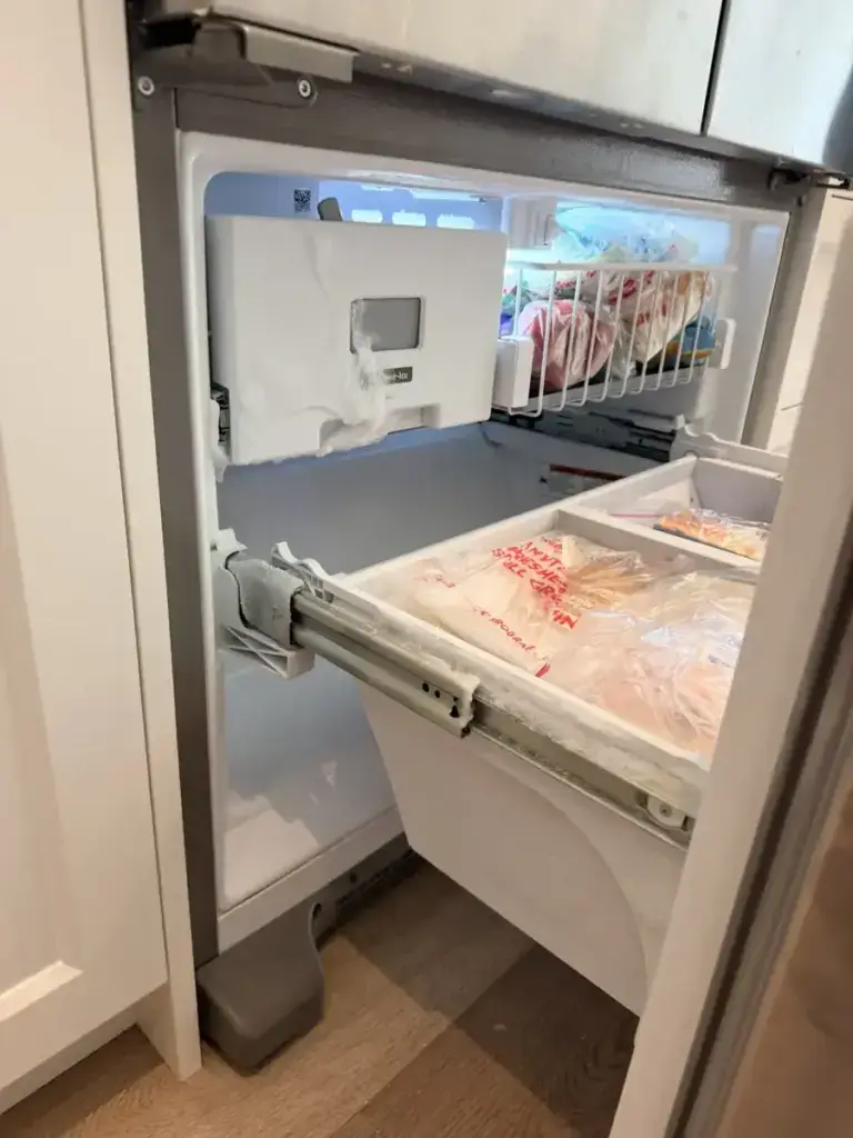 Interior of a refrigerator freezer drawer showing the ice maker above frozen food