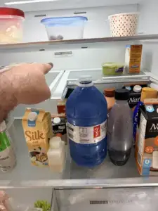 fridge repair technician pointing inside open whirlpool refrigerator stocked mil