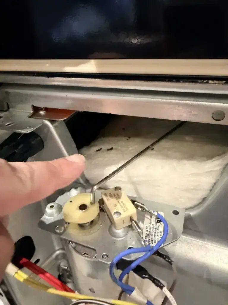 oven repair technician pointing oven door latch motor switch during repair
