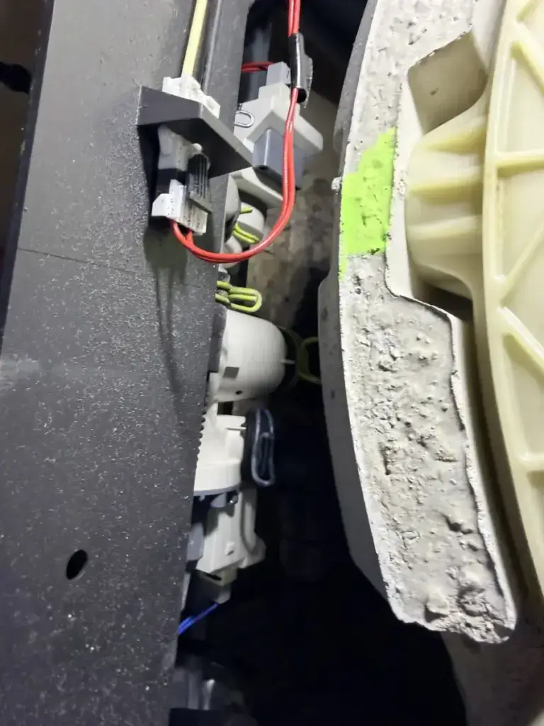 Close-up of a front-load washer's internal wiring connectors and concrete counterweight