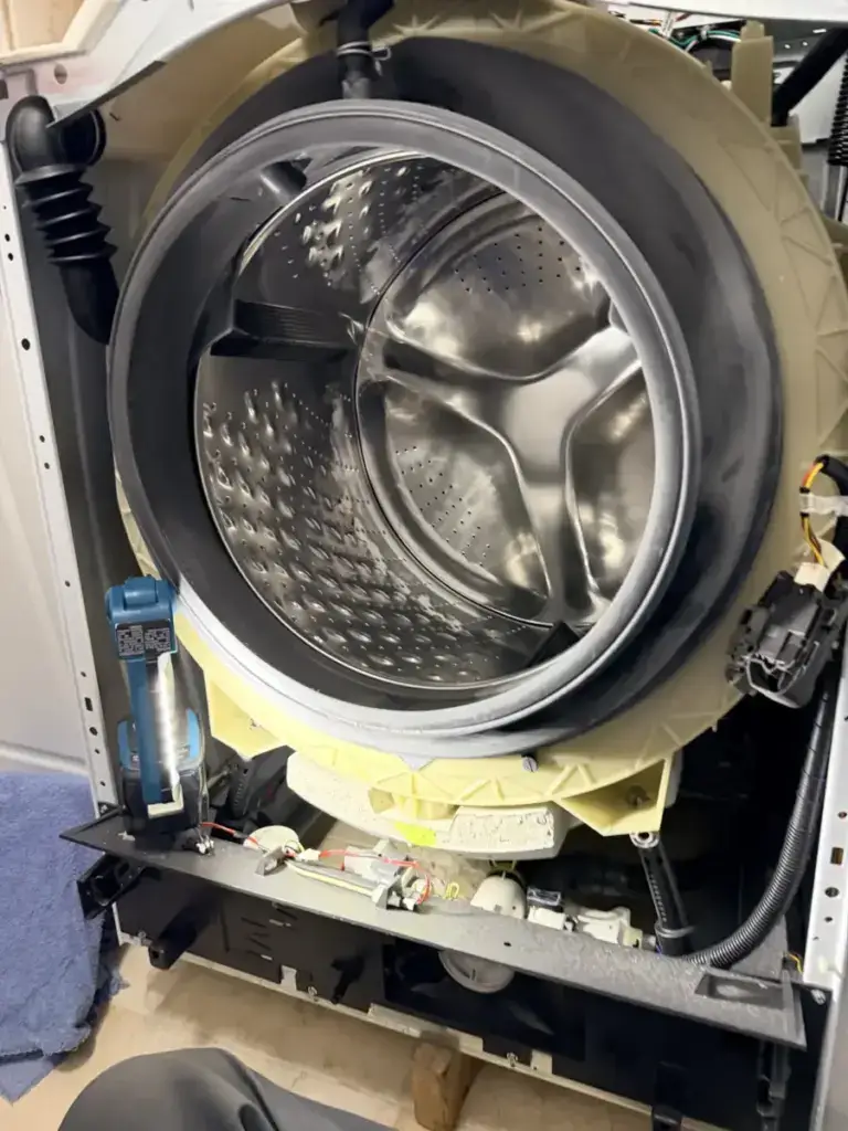 Open front-load washer with the stainless drum and outer tub exposed during a teardown repair