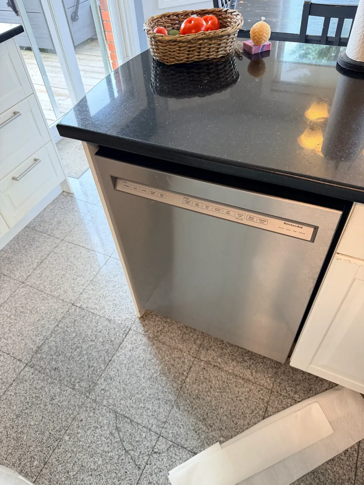 Stainless steel dishwasher in place under a dark counter with a sheet of paper on the tile floor in front