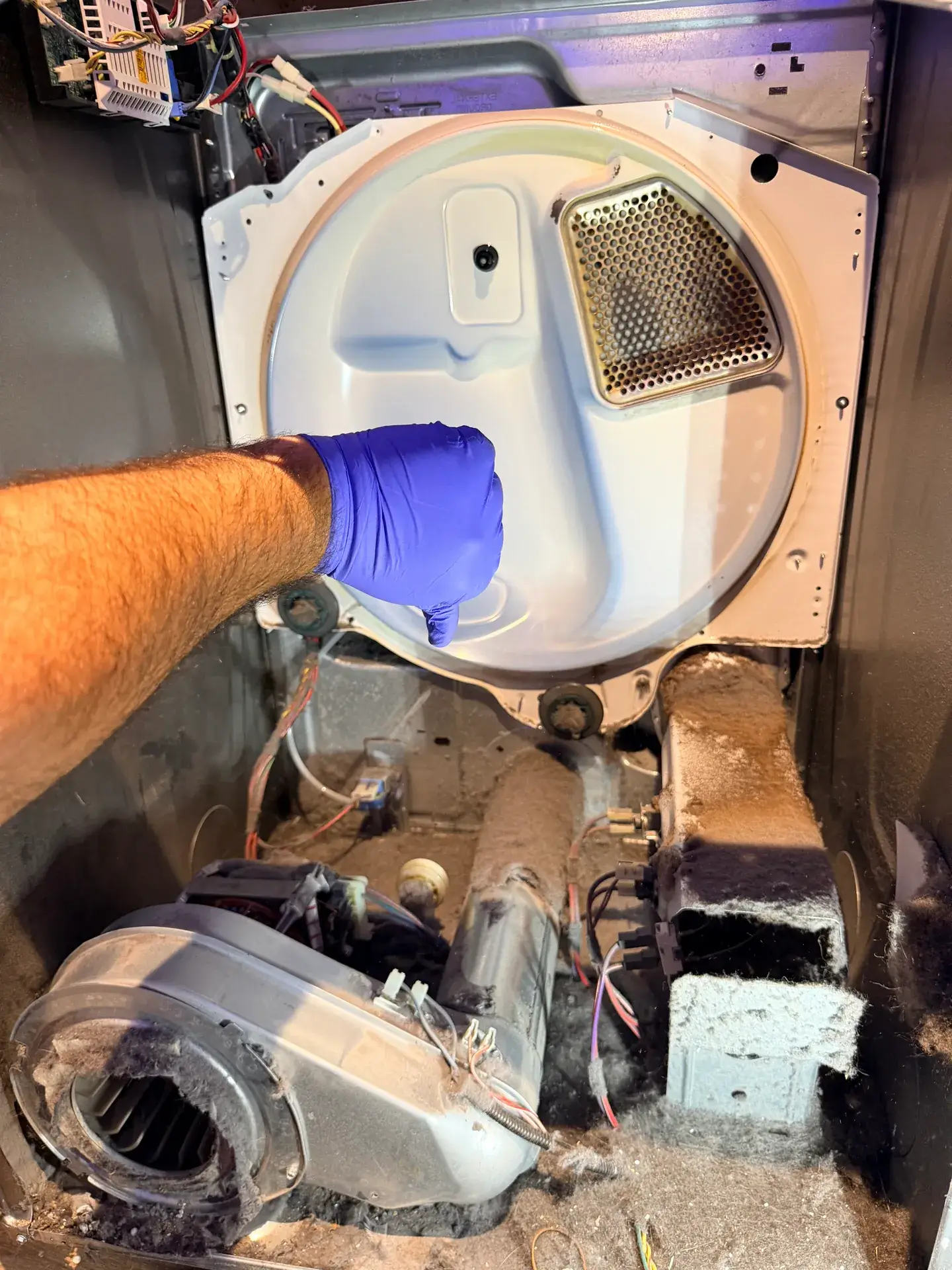 Dryer opened up in Barrie showing the blower housing and ducts coated in grey lint under the drum