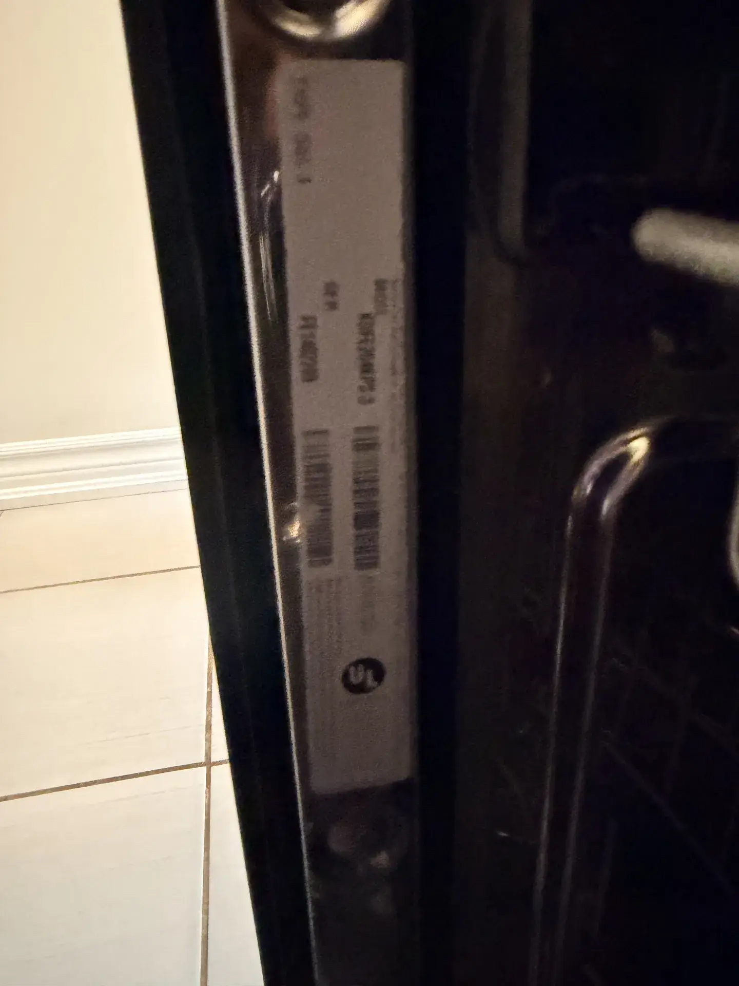 Rating label with model and serial lines and barcodes along the edge of a black refrigerator door, Alliston