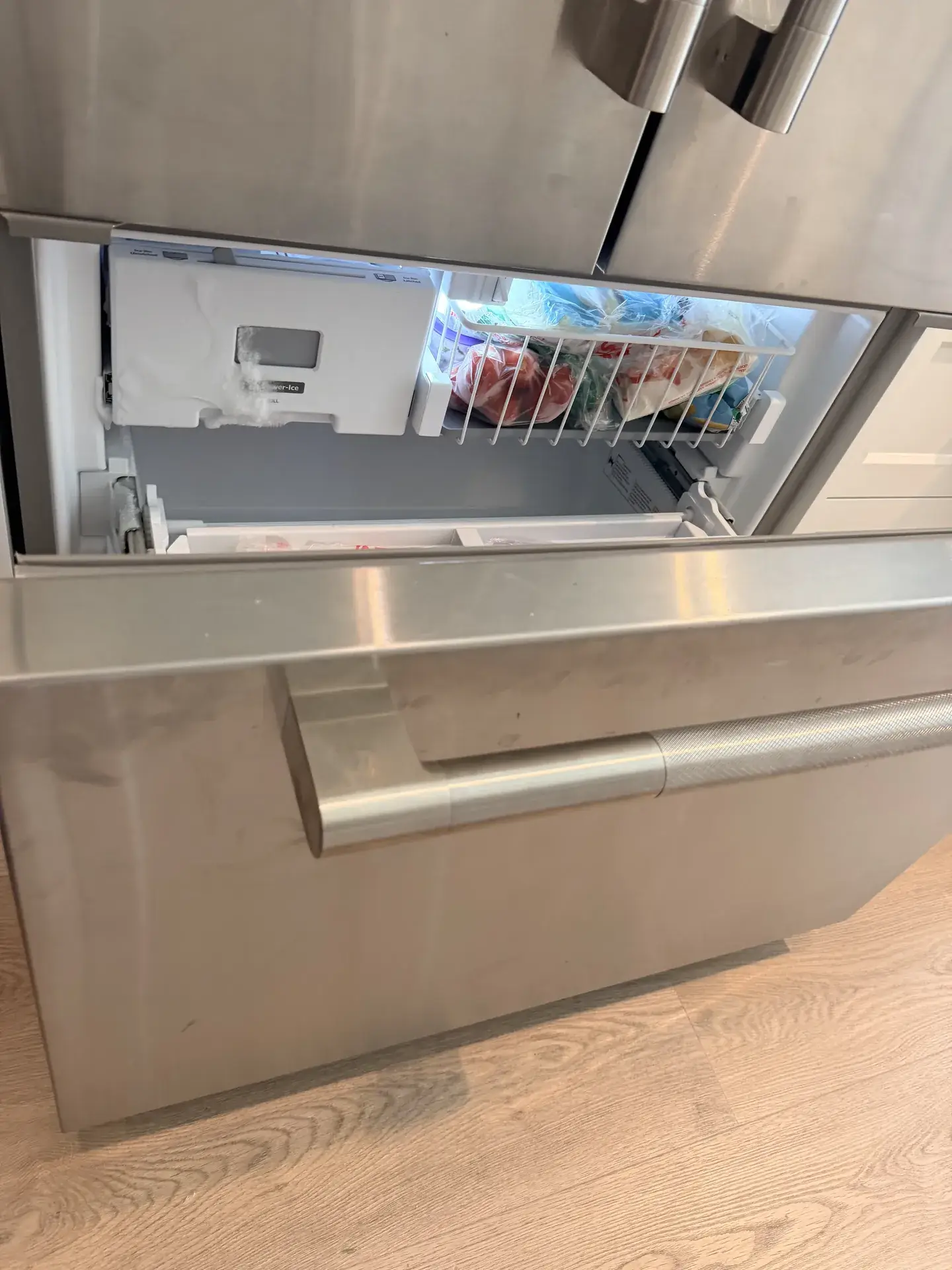 Bottom freezer drawer of a stainless French-door refrigerator open, with frost and ice coating the ice maker housing, Markham