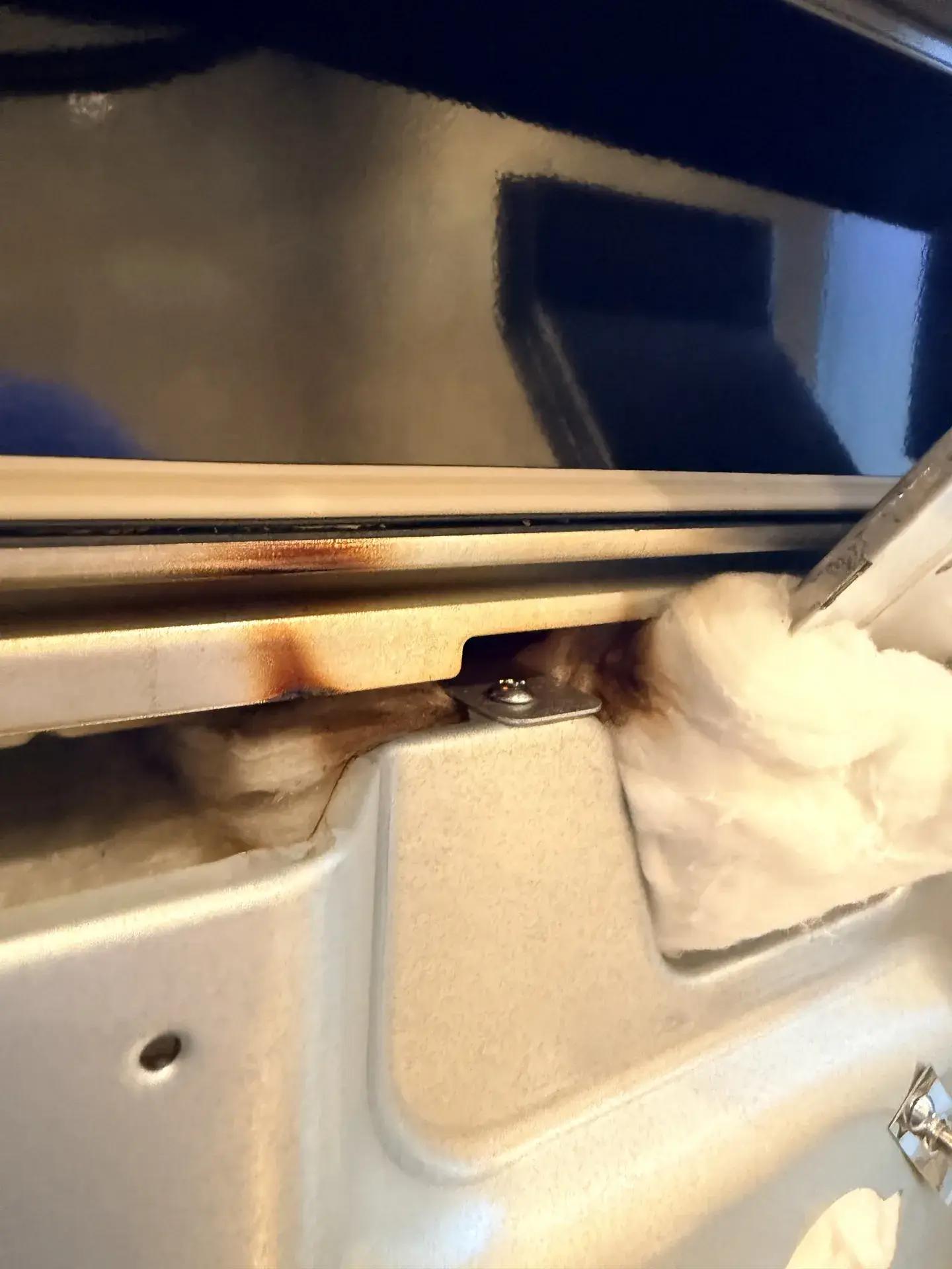 Scorch marks on the metal frame at the bottom of an oven opening with white insulation exposed, seen during an oven repair in Aurora