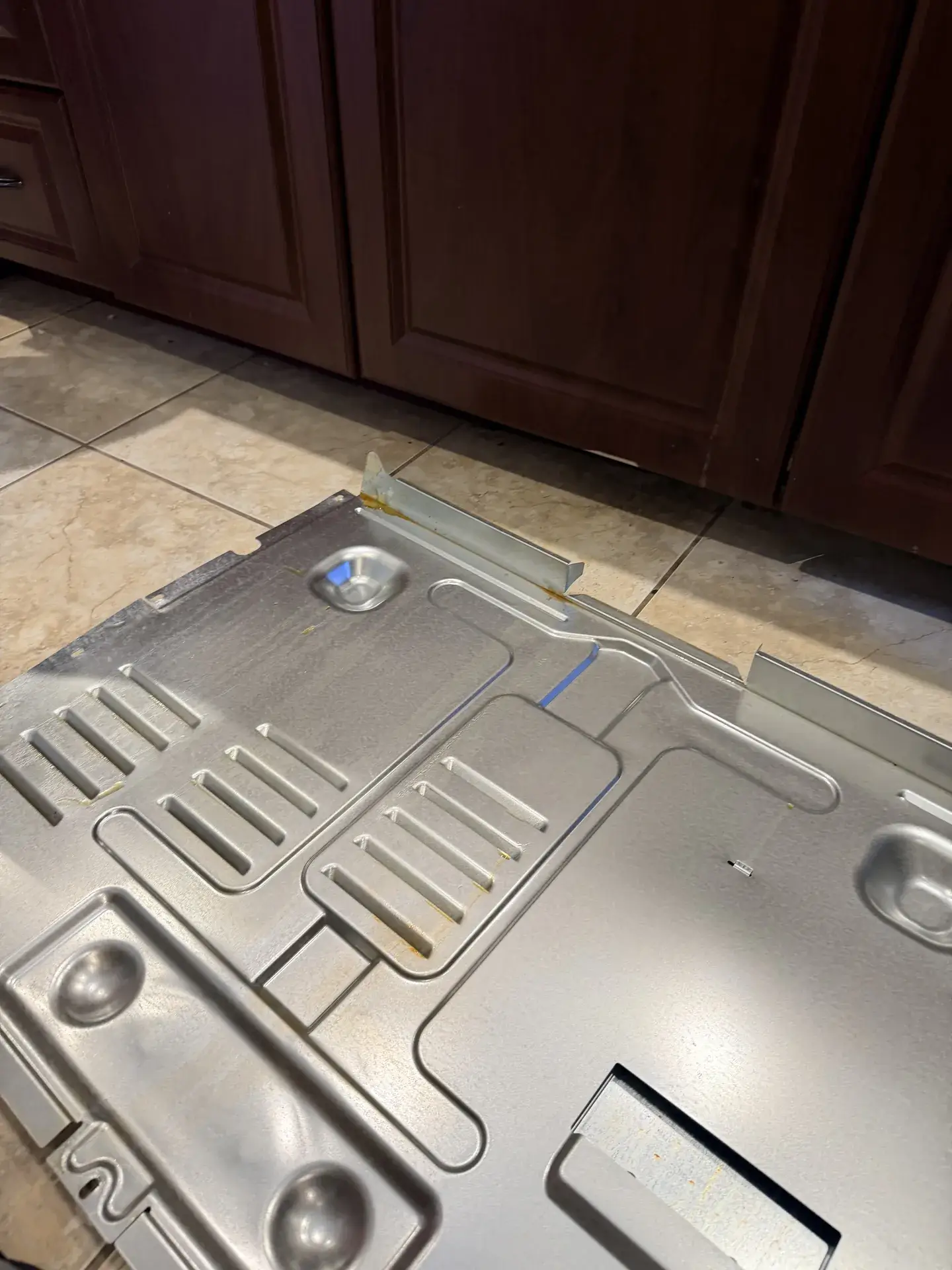 Stamped steel panel with raised ribs taken off a range during an oven repair, lying on a tiled kitchen floor in Aurora