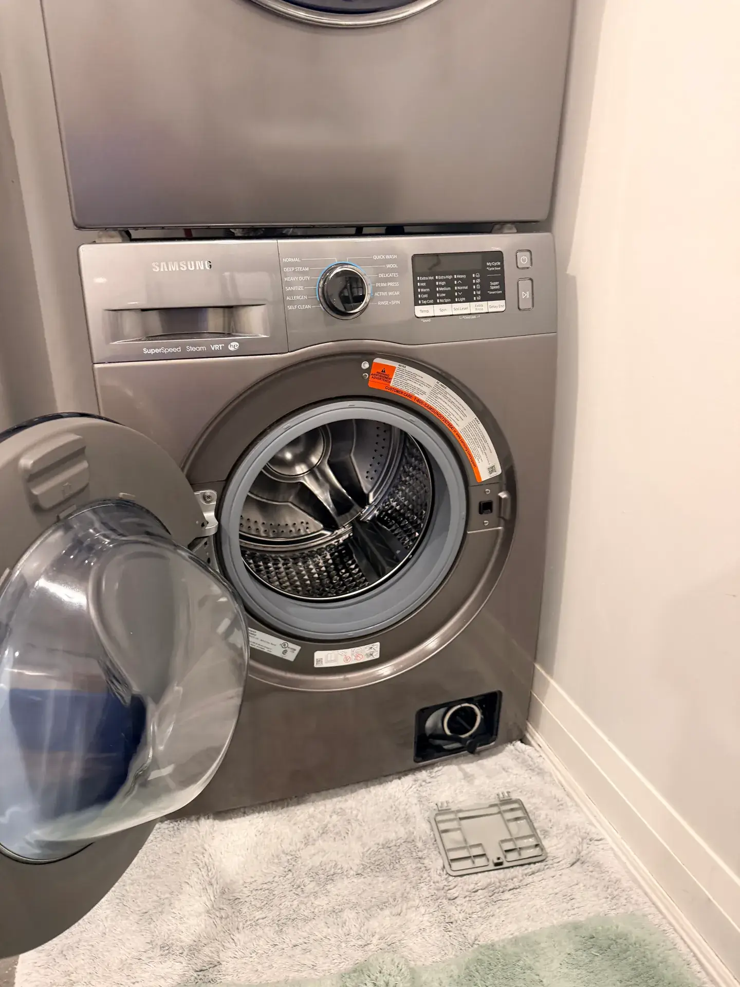 Samsung front-load washer with the door open and the small bottom access cover removed and lying on the mat, Toronto